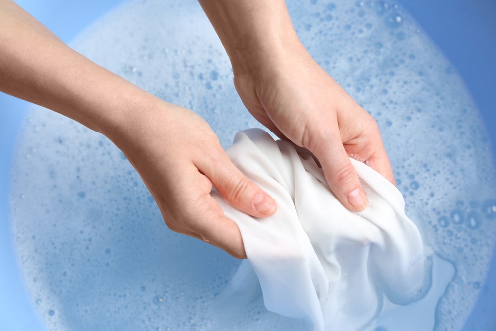 An overhead view of hands washing clothes in soapy water