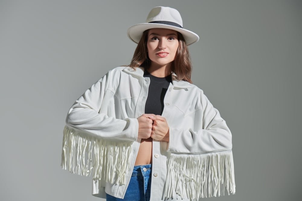 A charming smiling girl with long hair, in the style of the Wild West in jeans, a fringed jacket and a wide-brimmed hat.