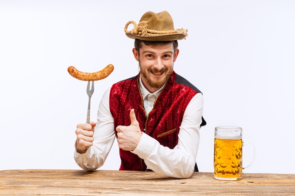 Portrait of Oktoberfest young man in hat, wearing traditional Bavarian or german clothes with beer mug and sausage