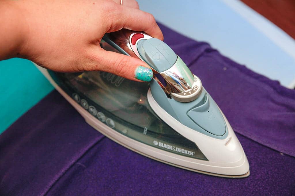 a girl using iron to remove sticker residue from a purple fabric