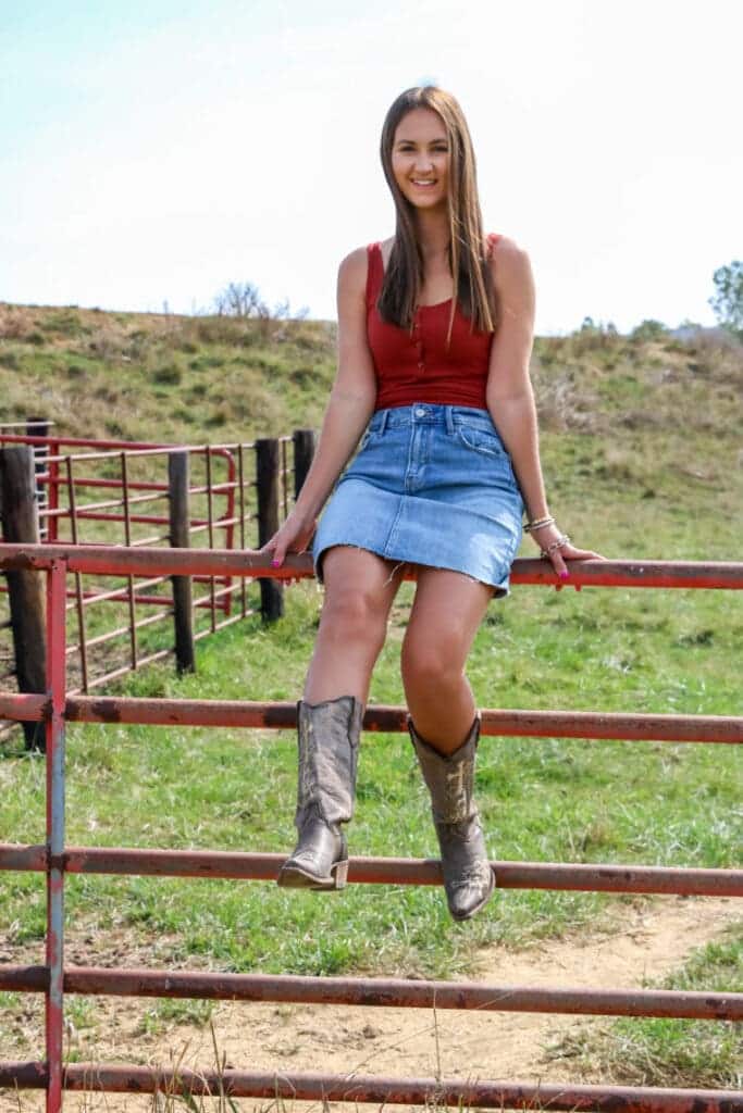 a young girl sittting on a fence with high waisted denim skirt