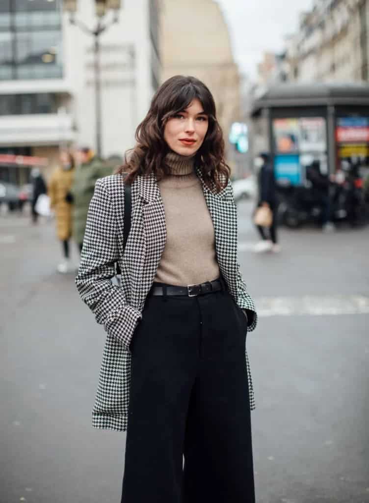 checkered black and white blazer styled by a woman standing holding a bag turtle neck and wideleg trousers