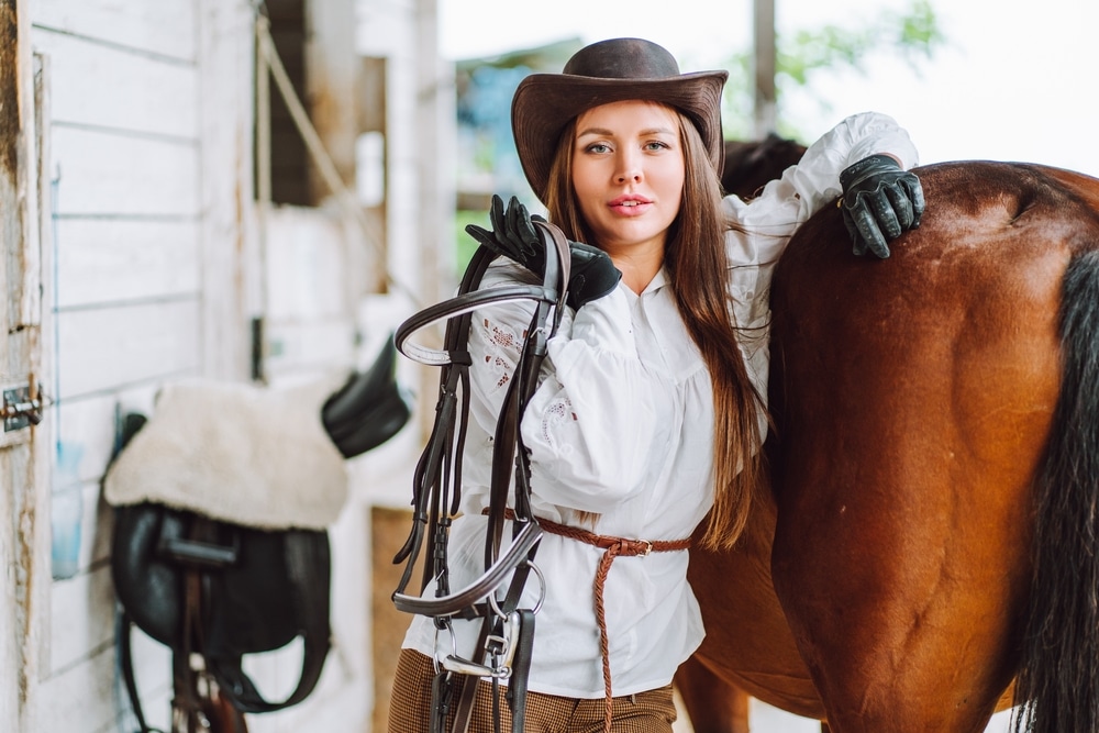 cowgirl wearing hat and gloves holding saddle