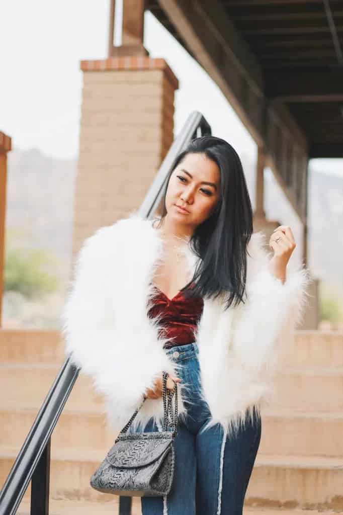 girl all glammed up in white furry coat jeans and red top holding a bag