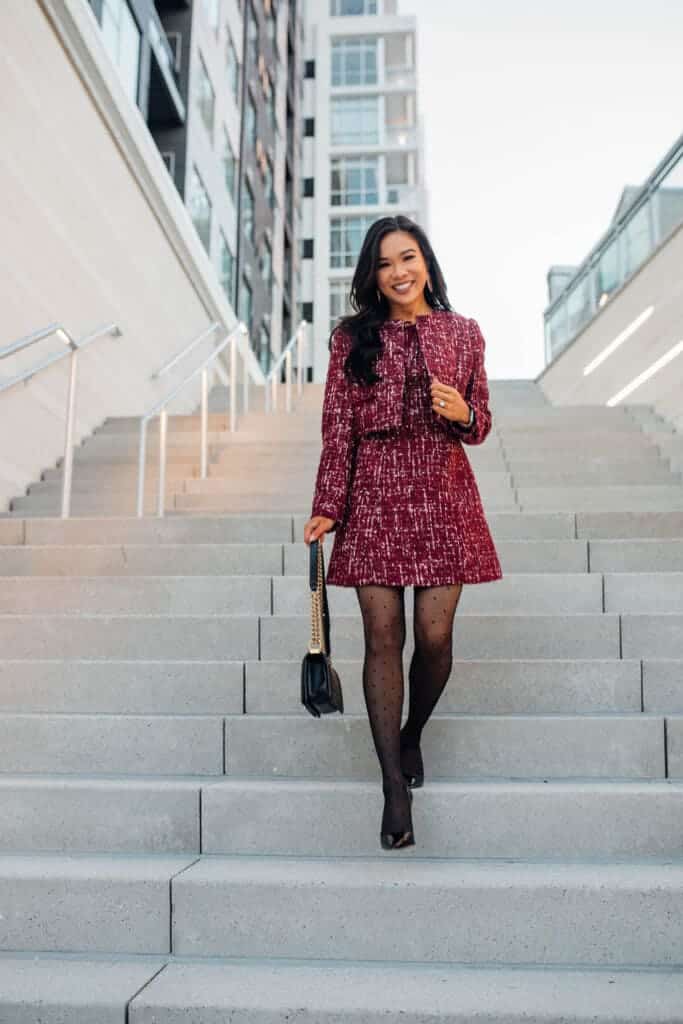 girl is standing on stairs posing for camera wearing tweed jacket and leggings holding a bag