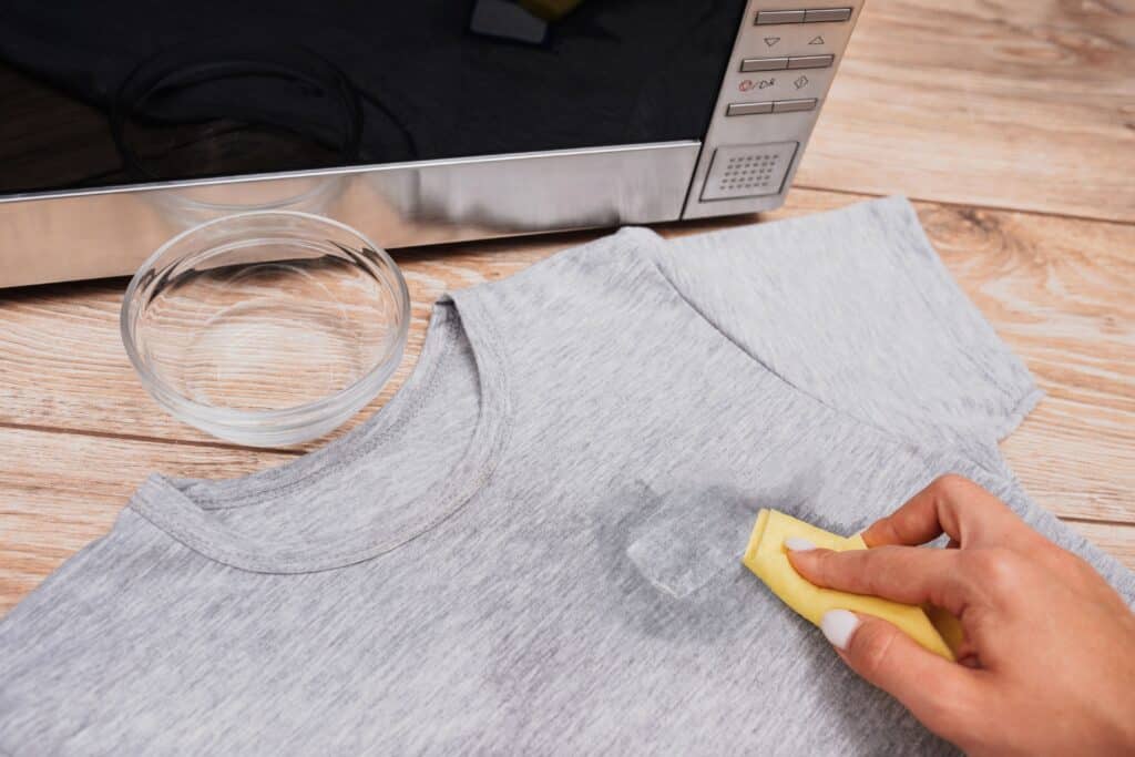 someone using oil to remove sticker glue from a shirt a bowl and cloth piece