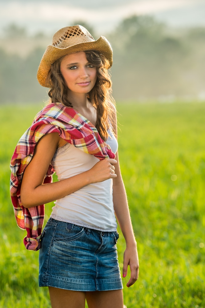  young woman wearing a straw hat and plaid shirt and denim skirt on the farm.