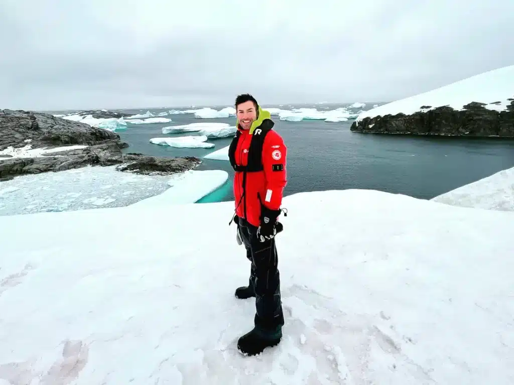 A guy standing in snow wearing black pants and red jacket