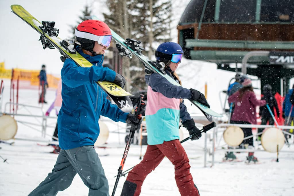 A side view of two people holding sledges and wearing ski clothes in snow