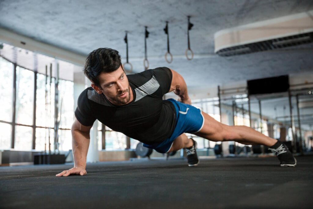 A view of a guy doing pushups with one hand wearing gym clothes