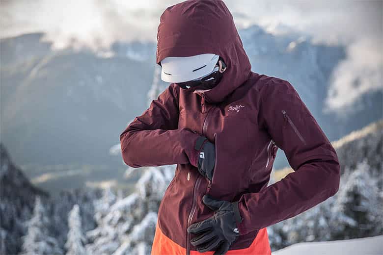 A view of a person wearing a maroon jacket with a backdrop of snowy mountains