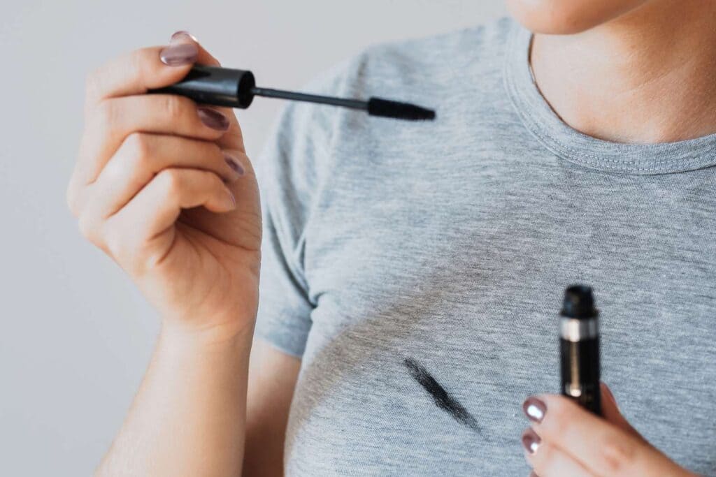 a girl holding a mascara and a stain on her shirt