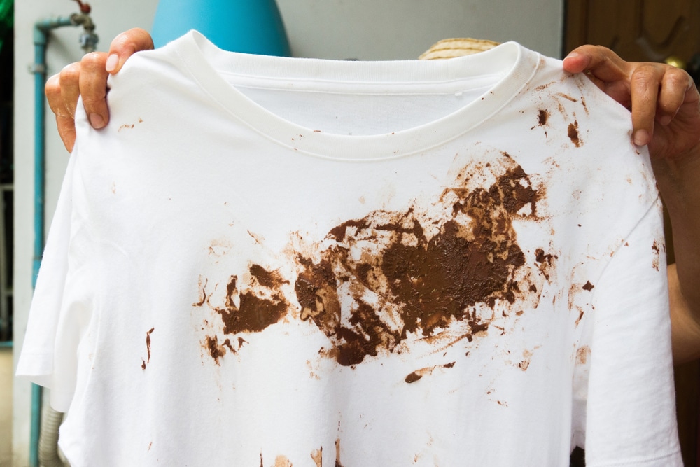 a woman holding a dirty white shirt with mud stains 
